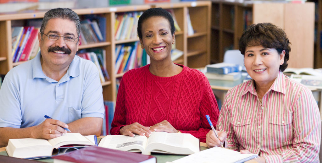 Three people sitting in library with books and notepads
